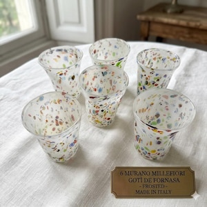 Peut inclure: Un ensemble de six verres dépolis ornés d'un motif confettis multicolore composé de petites taches. Une plaque rectangulaire couleur laiton porte l'inscription : 6 MURANO MILLEFIORI GOTÌ DE FORNASA - FROSTED - MADE IN ITALY.