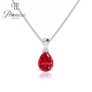 May include: A silver necklace with a teardrop-shaped, vibrant red gemstone pendant. The pendant is set in a silver setting and hangs from a delicate silver chain. The necklace is displayed against a white background.