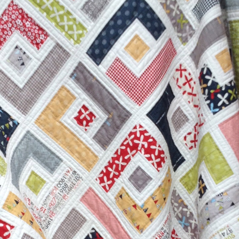 May include: A quilt with a geometric pattern in shades of red, white, gray, yellow, and green. The quilt is made of different fabrics with various patterns, including polka dots, gingham, and floral prints.