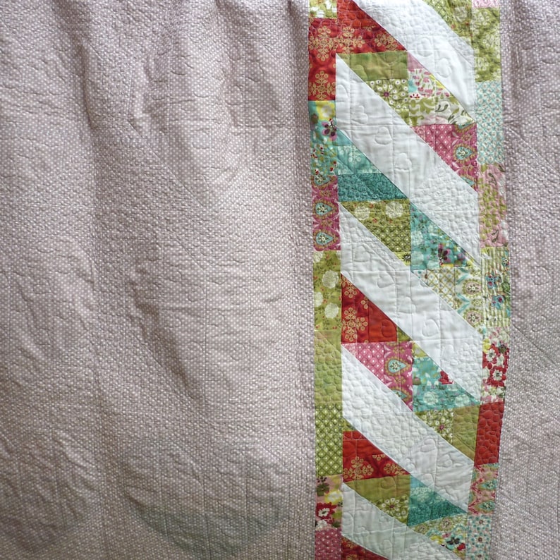 Pode incluir: Uma colcha rosa e branca com uma borda de patchwork colorida. A borda apresenta uma variedade de tecidos em tons de vermelho, verde, azul e rosa. O patchwork est&aacute; disposto em diagonal.