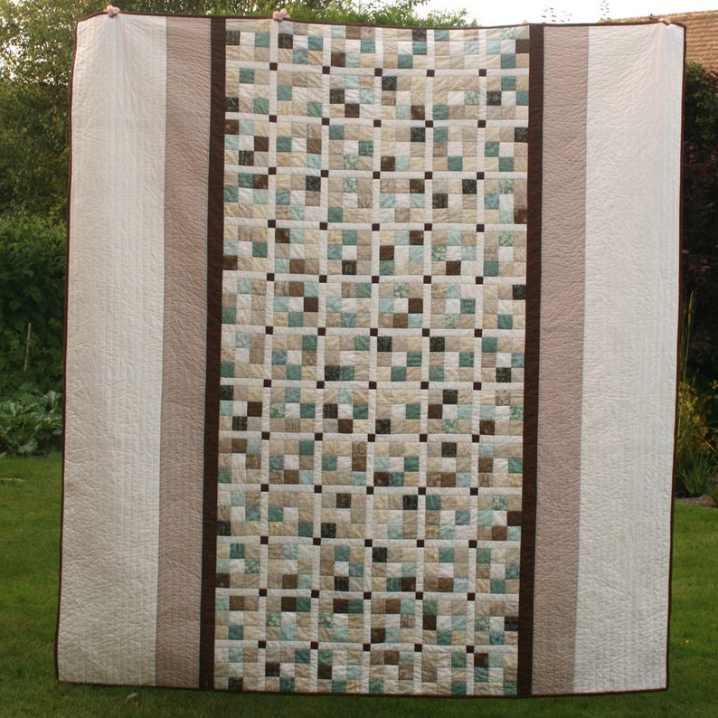 May include: A large quilt with a patchwork design featuring squares of various shades of brown, beige, and blue. The quilt is bordered with white and brown fabric.