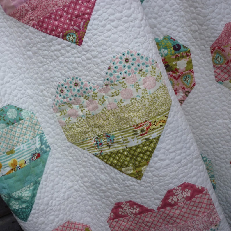 Pode incluir: Um edredom branco com um design de patchwork que apresenta cora&ccedil;&otilde;es em v&aacute;rias cores e padr&otilde;es. Os cora&ccedil;&otilde;es s&atilde;o feitos de diferentes tecidos com padr&otilde;es florais, geom&eacute;tricos e listrados. O edredom &eacute; acolchoado com um pequeno padr&atilde;o circular.