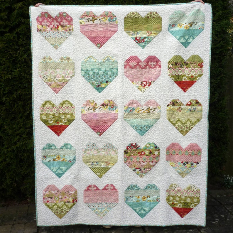 Pode incluir: Um edredom branco com um design de patchwork de 16 cora&ccedil;&otilde;es. Cada cora&ccedil;&atilde;o &eacute; feito de diferentes tecidos em tons de rosa, verde, azul e branco. O edredom &eacute; feito com uma variedade de padr&otilde;es florais e geom&eacute;tricos.