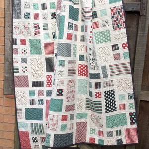 Op de afbeelding: Een wit quilt met een patchwork-ontwerp met verschillende geometrische vormen in rood, blauw en groen. Het quilt is gemaakt van verschillende stoffen met patronen zoals strepen, stippen en ankers.