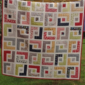 May include: A quilt with a geometric pattern of squares and rectangles in shades of red, white, gray, black, yellow, and green. The quilt is made of different fabrics with various patterns and textures.