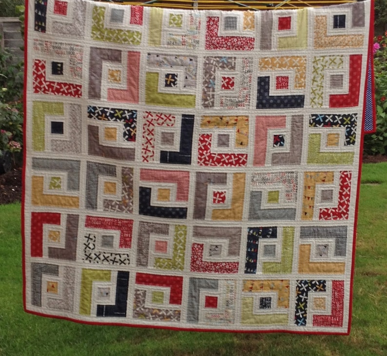 May include: A quilt with a geometric pattern of squares and rectangles in shades of red, white, gray, black, yellow, and green. The quilt is made of different fabrics with various patterns and textures.