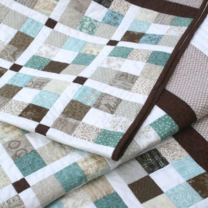May include: A quilt made of various fabric squares in shades of brown, beige, and blue. The quilt is folded in half, revealing the brown and beige fabric squares on the underside.