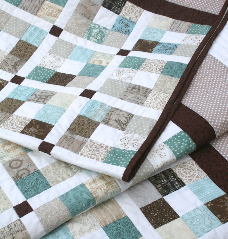 May include: A quilt made of various fabric squares in shades of brown, beige, and blue. The quilt is folded in half, revealing the brown and beige fabric squares on the underside.
