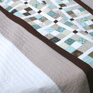 May include: A quilt with a brown border and a patchwork design of white, brown, and blue squares. The quilt is made with a variety of fabrics, including some with floral patterns.