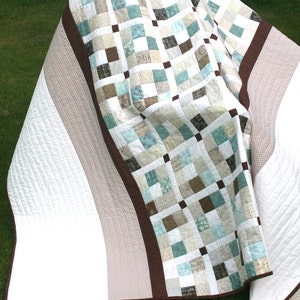 May include: A white and brown patchwork quilt with a brown border. The quilt is folded in half and the back side is visible. The back side is white with brown stripes.