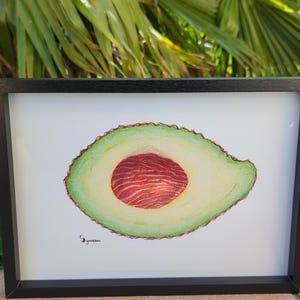 Peut inclure: Une peinture à l'aquarelle encadrée d'un avocat tranché, montrant la peau extérieure verte, la chair jaune-vert et une graine brun rougeâtre. L'œuvre est placée sur un fond blanc dans un cadre noir, idéale pour la décoration de cuisine ou de salle à manger.