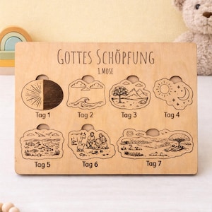 Op de afbeelding: Houten puzzel met de tekst "GOTTES SCHÖPFUNG" en "1.MOSE". De puzzel toont zeven stadia van de schepping, elk met een illustratie en het label "Tag" gevolgd door een nummer. De illustraties omvatten de zon, maan en diverse scènes.