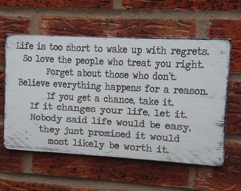 May include: White wooden sign with black text that reads: "Life is too short to wake up with regrets. So love the people who treat you right. Forget about those who don't. Believe everything happens for a reason. If you get a chance, take it. If it changes your life, let it. Nobody said life would be easy, they just promised it would most likely be worth it."