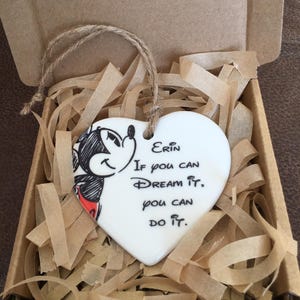 Peut inclure: Une décoration en céramique blanche en forme de cœur avec une illustration en noir et blanc de Mickey Mouse. La décoration a une ficelle en ficelle pour accrocher et le texte "Erin Si vous pouvez rêver, vous pouvez le faire."