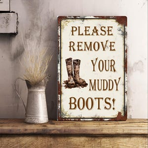 May include: A rectangular metal sign with a distressed finish, featuring the text "PLEASE REMOVE YOUR MUDDY BOOTS!". The sign has an image of muddy boots and is designed for a rustic or farmhouse aesthetic.