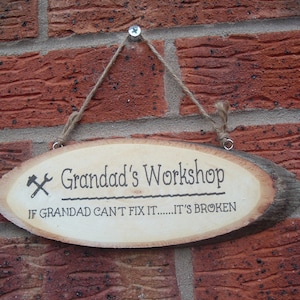 May include: A wooden sign with the text "Grandad's Workshop" and the phrase "If Grandad can't fix it.....it's broken". The sign is hanging from a brick wall with twine.