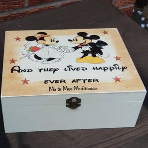 Op de afbeelding: Een witte houten doos met een scharnierend deksel. Het deksel is versierd met een cartoonafbeelding van Mickey en Minnie Mouse in trouwkledij. De tekst "And they lived happily ever after" is op het deksel gedrukt, samen met de namen "Mr & Mrs McDonagh".