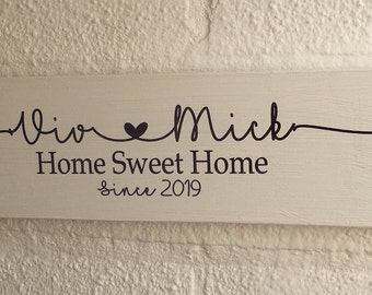 May include: White wooden sign with black lettering that reads "Viv & Mick Home Sweet Home since 2019". A heart symbol is between the names.