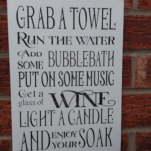Peut inclure: Une pancarte en bois blanc avec du texte noir qui dit "Prenez une serviette, faites couler l'eau, ajoutez du bain moussant, mettez de la musique, prenez un verre de vin, allumez une bougie et profitez de votre bain."