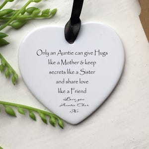 Peut inclure: Ornement blanc en forme de cœur avec texte noir. Le texte dit : « Seule une tante peut donner des câlins comme une mère et garder des secrets comme une sœur et partager l'amour comme une amie. » Un ruban noir est attaché pour l'accrocher.