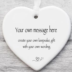 May include: A white heart-shaped ceramic ornament with a hole at the top for a ribbon. The text reads: Your own message here, create your own keepsake, gift with your own wording. A small line drawing of a heart with tiny hearts follows the text.