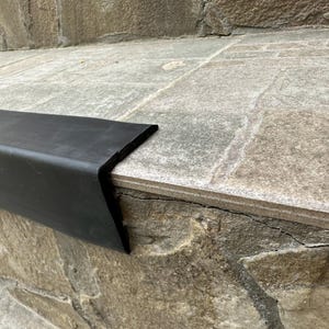 May include: Black rubber step edge trim fitted to a stone staircase. The trim is designed to prevent slipping and protect the edge of the steps.