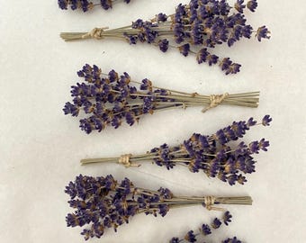 May include: Several bundles of dried lavender, each tied with twine. The lavender has a deep purple hue, and the stems are a light brown color. The bundles are arranged on a white surface, creating a simple and natural aesthetic.