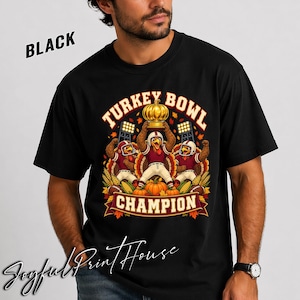 May include: A black t-shirt featuring a graphic of three turkeys dressed in football uniforms. The centre turkey holds a golden pumpkin trophy above its head. The text reads TURKEY BOWL CHAMPION, surrounded by autumn leaves, corn, and pumpkins.