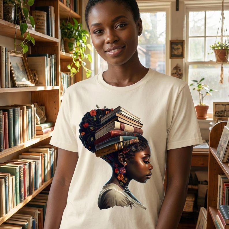 May include: A cream-colored t-shirt featuring a graphic of a woman with a stack of books on her head, adorned with flowers. The woman's profile is detailed with vibrant colors. The background includes bookshelves filled with books.
