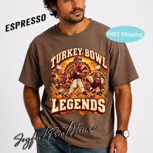 May include: A brown short-sleeve t-shirt featuring a graphic print of three anthropomorphic turkeys dressed in football uniforms. The text reads TURKEY BOWL LEGENDS. The design includes footballs, pumpkins, and autumn leaves in warm tones.