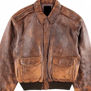 Könnte beinhalten: Eine braune Lederbomberjacke mit Reißverschluss und zwei großen Taschen. Die Jacke hat einen abgenutzten und verwitterten Look.