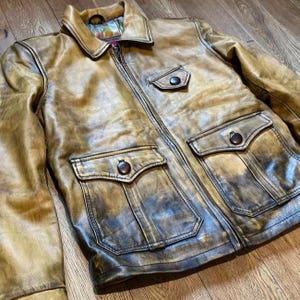 May include: A brown leather jacket with a zip fastening and two large flap pockets. The jacket has a distressed look and is made of a soft, supple leather.