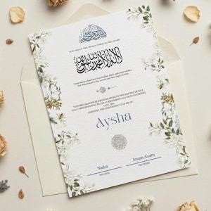 May include: A white invitation card with floral accents and Arabic calligraphy. The card includes the name "Aysha" in a stylish font, along with the names of witnesses. The invitation is placed inside a cream-colored envelope.
