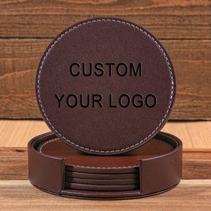 Puede incluir: Un juego de posavasos redondos de cuero marrón con costuras blancas y las palabras "CUSTOM YOUR LOGO" en relieve en el posavasos superior. Incluye un soporte a juego.
