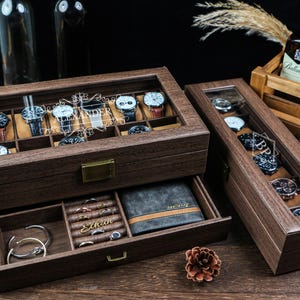May include: A brown wooden watch display case with a glass lid, showcasing various watches. The box includes a drawer with jewellery and a wallet. The watch box is personalised with the name "Alexander".