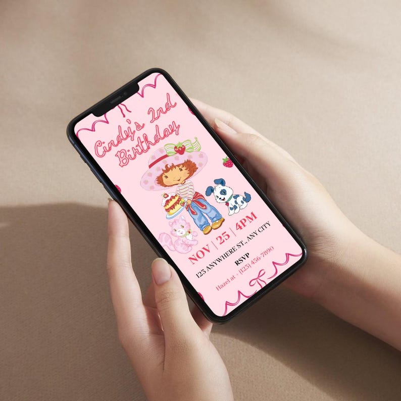 May include: A smartphone displays a pink birthday invitation. The invitation features a cartoon illustration of a girl with a strawberry hat, holding a cake, with a cat and a dog. The text reads "Cindy's 2nd Birthday" and includes date, time, and RSVP information.