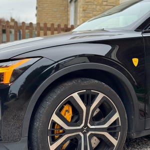 May include: A black car with yellow brake calipers and a yellow emblem on the side. The car has black wheels with silver spokes.