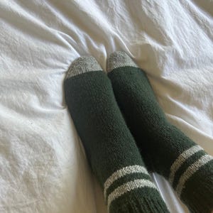 May include: A pair of green socks with white stripes. The socks are made of a soft, fuzzy material.