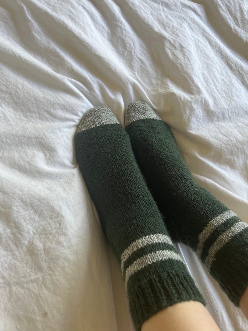 May include: A pair of green socks with white stripes. The socks are made of a soft, fuzzy material.