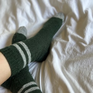 May include: A pair of green socks with white stripes. The socks are made of a soft, fuzzy material.