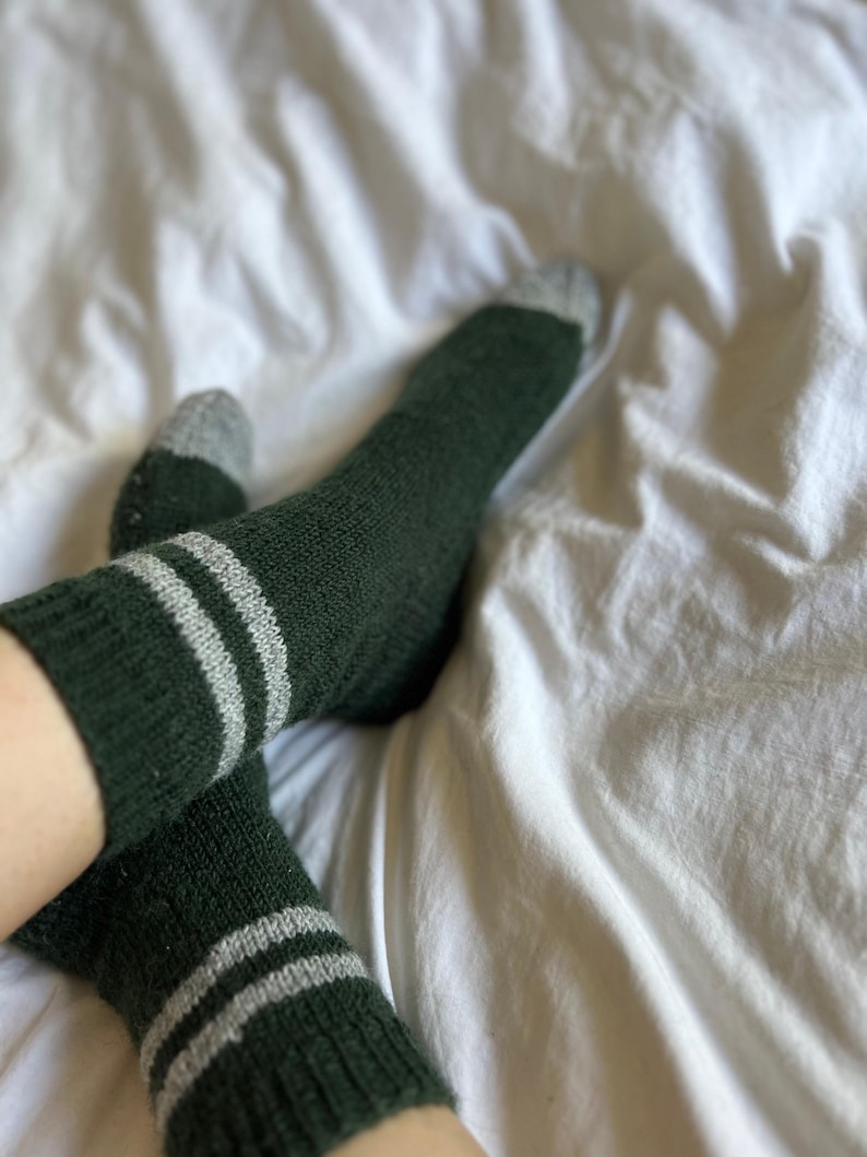 May include: A pair of green socks with white stripes. The socks are made of a soft, fuzzy material.