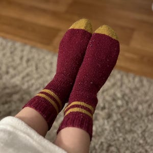 May include: A pair of red socks with gold stripes. The socks are made of a soft, fuzzy material.