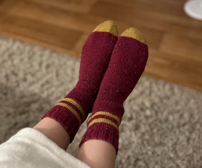 May include: A pair of red socks with gold stripes. The socks are made of a soft, fuzzy material.