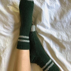 May include: A pair of green socks with white stripes. The socks are made of a soft, knitted fabric and have a grey toe and heel.