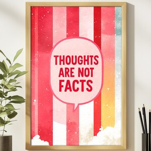 May include: A framed art print with the text "THOUGHTS ARE NOT FACTS" in a speech bubble. The background features vertical stripes in shades of red, pink, and white, with a touch of blue and yellow. The frame is a light wood color.