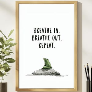 May include: A framed wall art print featuring a green frog sitting on a gray rock. Above the frog, the text reads: BREATHE IN. BREATHE OUT. REPEAT. The print is enclosed in a light-colored wooden frame, presenting a clean and simple visual composition.