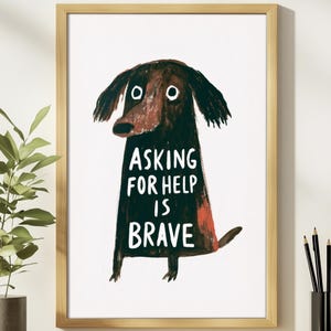 May include: A framed wall art print featuring a dark brown, stylized dog illustration on a white background. The dog has large, wide eyes and the text "ASKING FOR HELP IS BRAVE" is printed in white capital letters across its body.