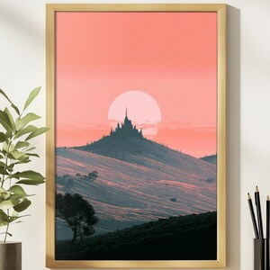 May include: A framed wall art print featuring a silhouette of a castle atop a rolling hill against a large, pale pink sun. The sky is a gradient of coral and peach tones, while the landscape below is rendered in dark, textured shades of blue.