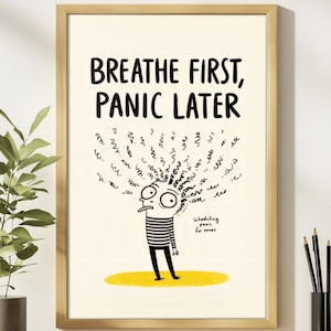 May include: A framed wall art print featuring a cartoon character with messy hair and the text "BREATHE FIRST, PANIC LATER" at the top. Below the character, smaller text reads "Scheduling panic for never." The character stands on a yellow oval.