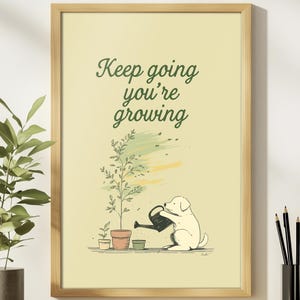 May include: A framed art print with a light yellow background. The print features a cartoon dog watering a plant, with the text "Keep going you're growing" in green script. The frame is made of light brown wood.